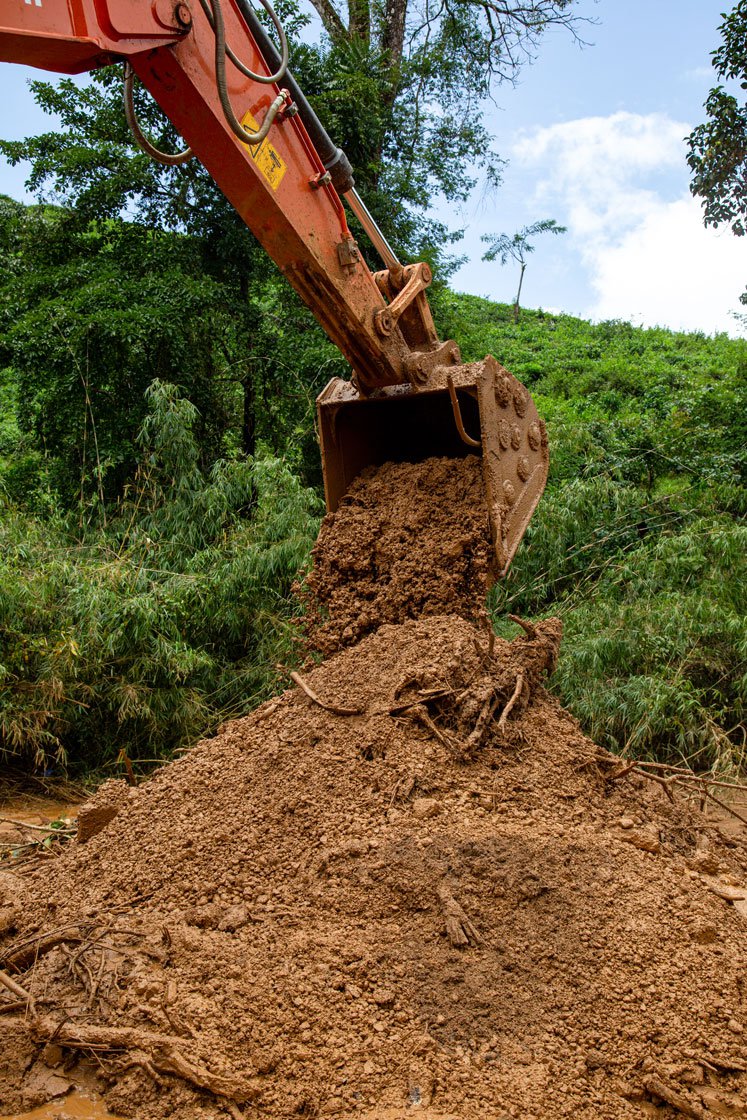 Machines (left) are helping move soil and find people. A volunteer (right) searches for bodies along the river