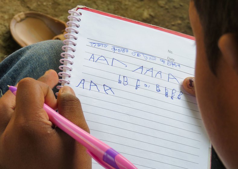 Prateek Raut on the porch of his home in Rashin village and writing in a notebook, in October 2020. He is learning the alphabet and numbers from the beginning at his school now