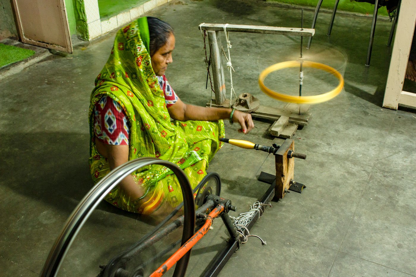 Fifty-five-year-old Gangaben Parmar of Ghaghretia village takes the silk thread from the hank onto a big wooden spool, and from there with the help of a spinning wheel she carries the thread onto a bobbin. 'I have been working for thirty years. I have some difficulty in vision these days. But if I sit here all day long I can wind 20 or 25 bobbins in a day'