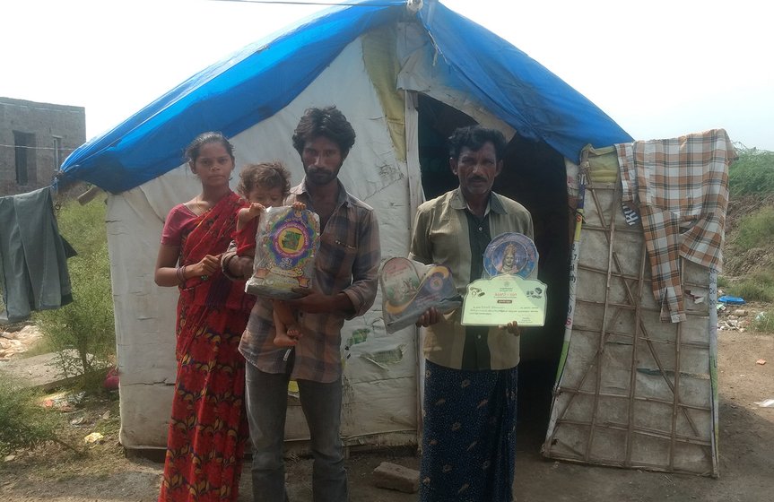 A man and his family stand outside their hut