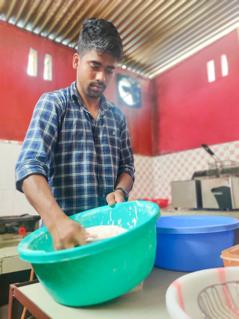 Biman dredging marinated chicken in flour (left) and slicing onions (right) to prepare a burger