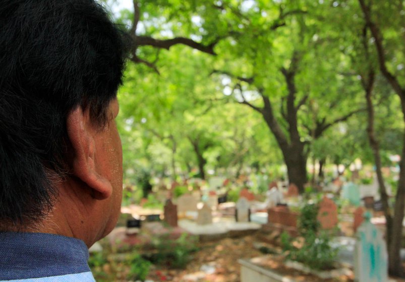 Left: From across the graveyard, you can see the building of the Delhi police headquarters at ITO. Right: Nizam has been printing names of the deceased on these gravestones for over 40 years