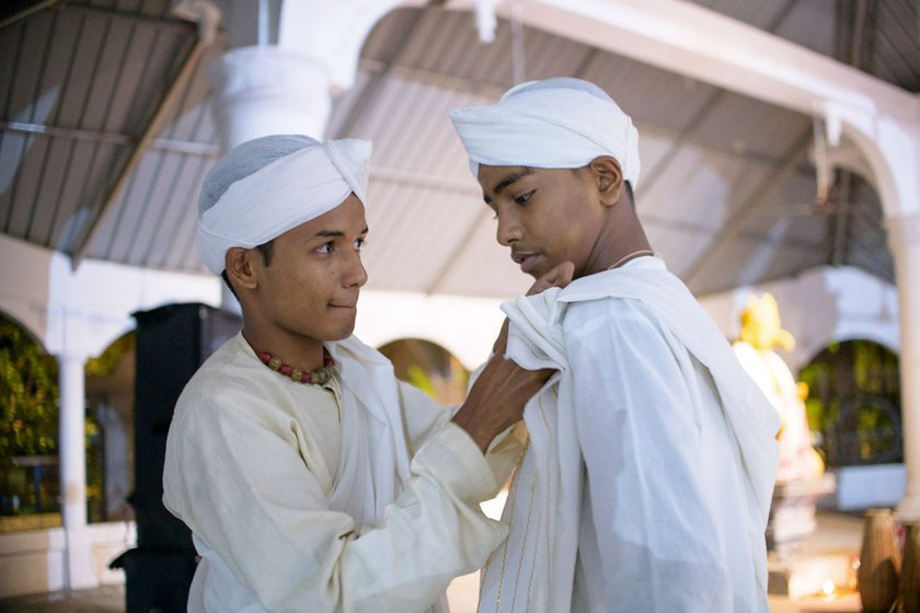 Right: Priyabrat helps Siddhartha Borah pin the seleng sador to his shoulder. The seleng is a long, rectangular piece of cloth draped over the body and makes an essential part of the performance attire