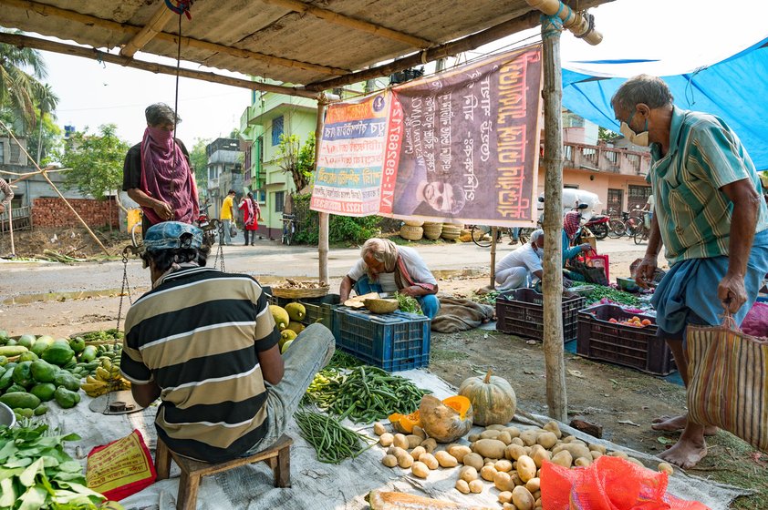 Left: For 23 years, 47-year-old Prafulla Debnath has been doing odd jobs at the regular Samabay Krishi Unnayan Samity Market (now closed for the lockdown). He carries sacks to be delivered to the houses of customers, and carries goods from vehicles to shops. And he sweeps the whole market – picking up Rs. 2 per day from each vegetable vendor and Re. 1 per day from the other shopkeepers. But now, with the market shifted to the field in Dutta Para, even his bare earnings have halved, though some of the vegetable vendors arrange for breakfast and lunch for Debnath. “If I do not clean, the market will be dirty,” he says. “If I clean the market then everyone will know my name. Nobody will work like me!” Right: Since the market is open for only a few hours, many buy at the last minute, hoping for low prices. Khoka Roy, 50, was a carpenter, then he ran a small grocery shop from home, and is now out selling in the market due to the lockdown. From Rs. 400-500 per day, his income has dropped to Rs. 200-250. “With the police patrolling, people are not leaving their houses,” he says. “You tell me, how we can sell vegetables?"

