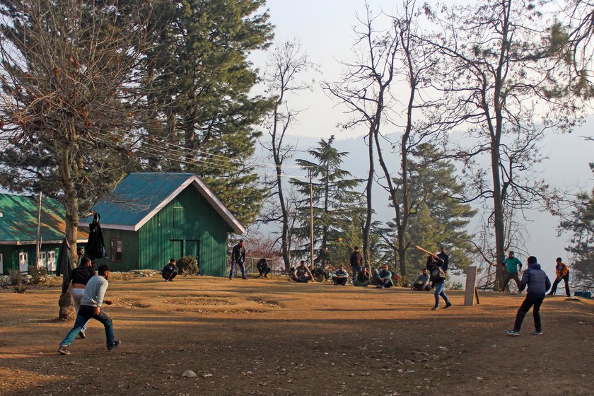 Employees of clothing rental shops watch videos on their mobile phones (left) or play cricket in a nearby ground as they wait for work