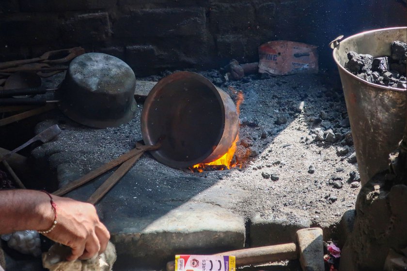 The thathera heats the utensil over the flame, ready to coat the surface .