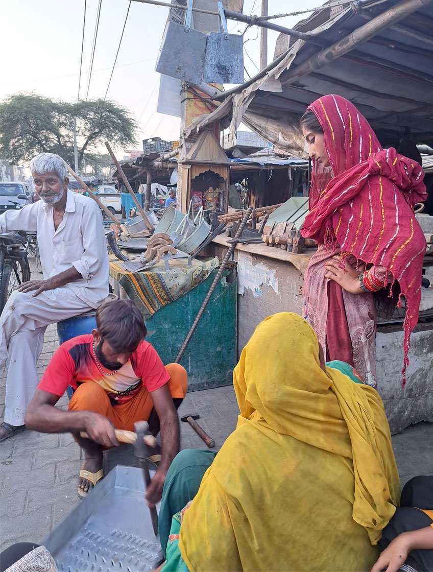 Nine-year-old Chidiya uses a hand-operated fan to blow the ashes away from the unlit bhatti . The family earn much less these days than they did just a few years ago – even though they work in the middle of a busy market, sales have been slow since the pandemic