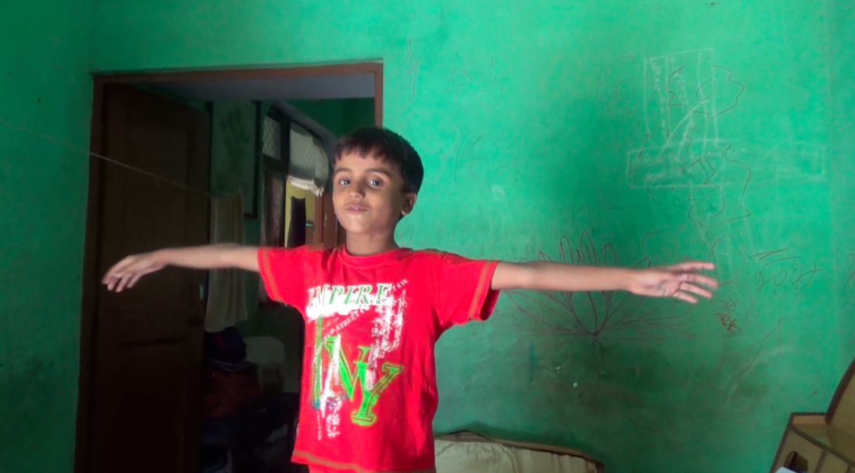 Tamannag standing with her hands outstretched in front of green wall